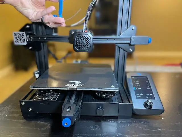 A hand cutting approx 100mm of extruded filament hanging out of an Ender 3 V2 extruder.