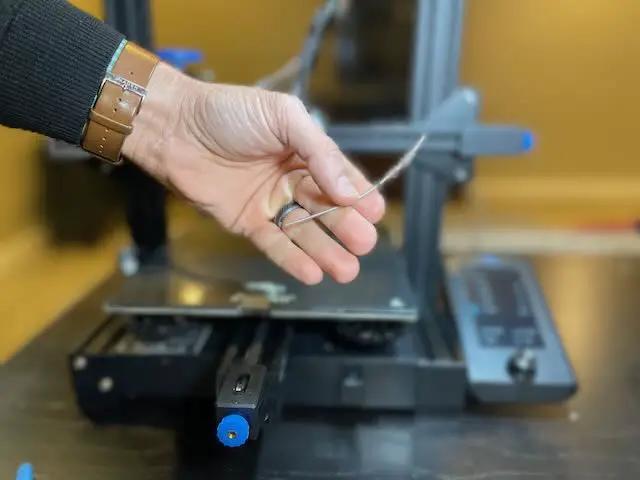 A hand holding approx 100mm of filament extruded from an Ender 3 V2