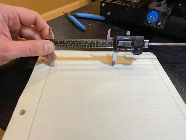 Calipers measuring markings on a piece of paper showing 98.5mm