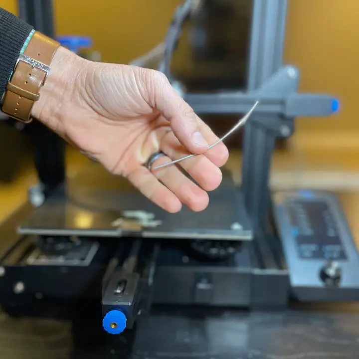 Man holding a piece of filament while quickly calibrating an ender 3 v2 e steps